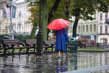 Lviv, Ukraine - September 30, 2020: senior woman wearing Nike sneakers and red umbrella walking on rainy street