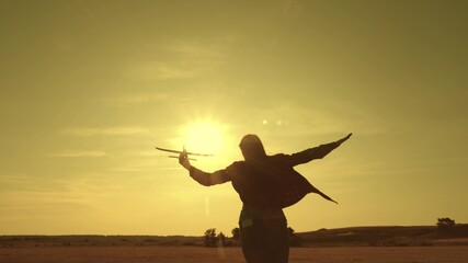 girl wants to become pilot and astronaut. Slow motion. Happy girl runs with a toy airplane on field in the sunset light. children play toy airplane. teenager dreams of flying and becoming pilot.