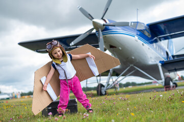 A cute little girl dressed in a cap and glasses of a pilot on the background of an airplane. The...