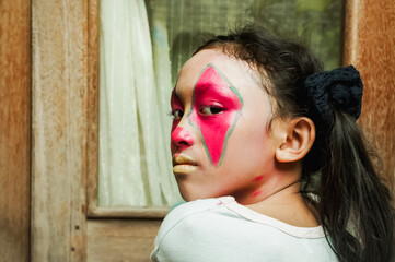 Mad expression of Asian little girl with clown make-up