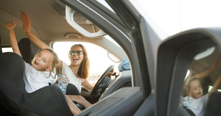 Donna al volante con maglietta bianca in contesto vacanziero viaggia con la figlia con espressioni...