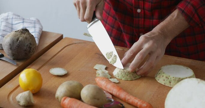 Vegetable soup preparing, peel off slice of celery root at cutting board using sharp knife, close up