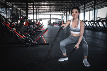 Obraz na płótnie Canvas Asian strong woman exercising with battle ropes,A female workout alone at the gym