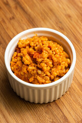Home cooked bulgur pilaf in a white ceramic portion cup on a kitchen wooden board top view