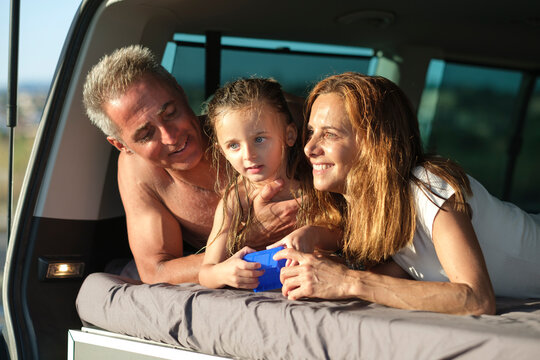 famiglia famiglia felice composta da pap&agrave; mamma e figlia, in abbigliamento da mare composta da pap&agrave; mamma e figlia, in abbigliamento da mare si abbraccia felice vicino al furgone in mezzo a una strada