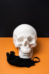 Masked plaster skull beside black mask. A minimalistic art concept dedicated to the pandemic. Black mask on a white plaster head.