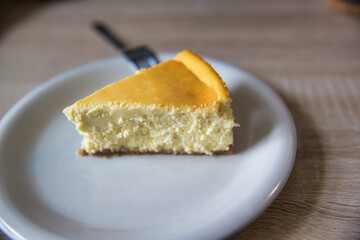 Slice of new york cheesecake on a white plate with fork. Depth of field