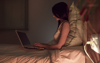 Young woman working on her laptop in bed before going to sleep.