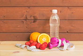 Dumbbells, bottle of water, fresh oranges, strawberry and measure tape. View with copy space.