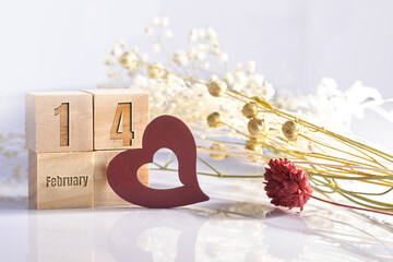 Wooden heart on white surface, February 14th marked on wooden blocks with colored preserved flowers.