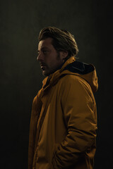 Fototapeta premium Shadowy portrait of blonde man in yellow coat in front of grey wall.