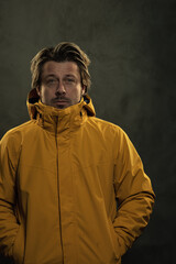 Blonde man in yellow coat in front of grey wall.