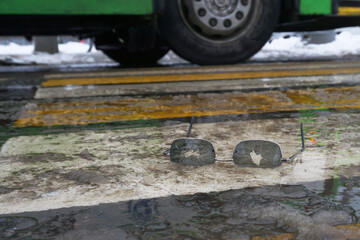 Broken glasses lie on an icy pedestrian crossing in background of a large wheel of a passing bus. Concept of the danger of slipping and falling on icy roads in winter.
