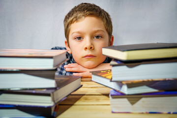 Portrait of a sad boy lying among children's books, standing on a wooden table.