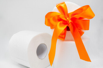 Several rolls of white perforated toilet paper. One roll is tied with a bright orange satin ribbon as a gift