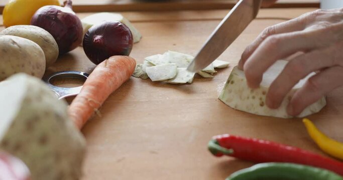 Vegetable soup preparing, peel off slice of celery root at cutting board using sharp knife, close up
