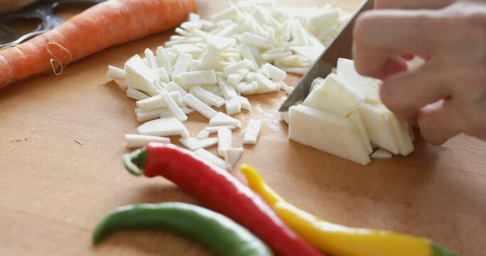 Vegetable soup preparing, chopping celery root at cutting board using sharp knife, close up