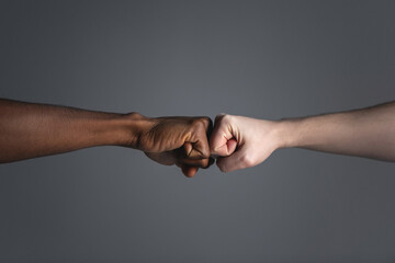 Close up of white skinned man and dark skinned man doing a fist bump.