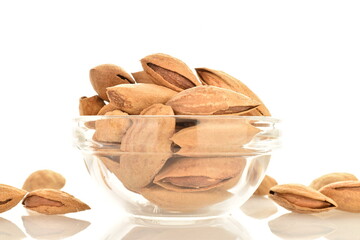 Dried unpeeled almonds in a glass bowl, close-up, isolated on white.