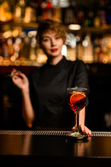 glass with bright alcoholic cocktail decorated with orange slice stands on bar