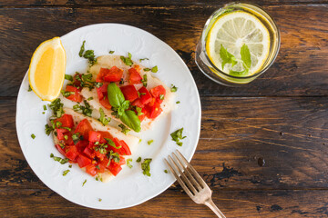 Halibut fish fillet baked with tomatoes. White plate, lemon, green basil, top view, close-up - 410474659
