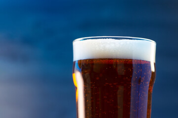 Close-up of a pint of beer on a blue illuminated background in the bar and copy space