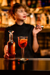 view on glass of bright cocktail on bar and bottle in hand of bartender nearby