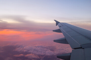 Fototapeta premium Wing of airplane above clouds in vivid colors sunset light.