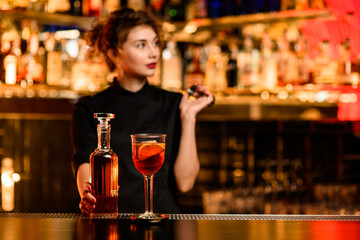 view of glass with cocktail on bar and bottle with drink in hand of bartender nearby