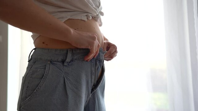 Overweight woman wearing jeans on fat body belly paunch. Young woman cannot button up jeans on her belly. The problem of excess weight, exercises for the press, sports load