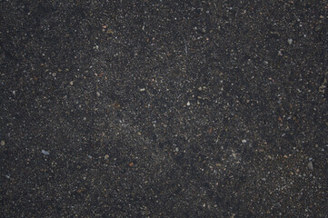 Direct overhead shot of the rough texture of dark asphalt filled with small stones that look like a starry sky. 