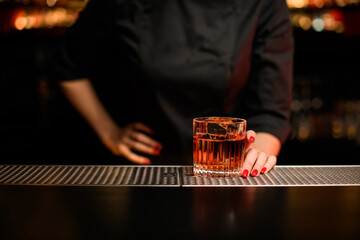 glass with drink on bar counter and hand of woman bartender is holding it