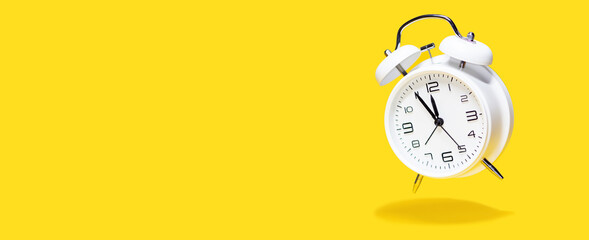 White bell alarm clock hovering over yellow background. 5 to 12 clock concept isolated - obrazy, fototapety, plakaty