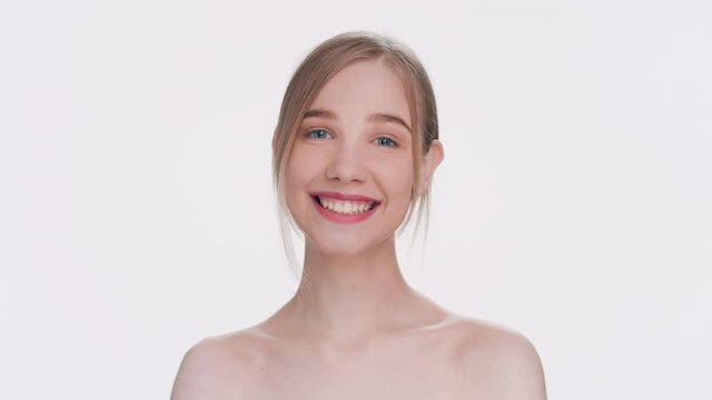 Young attractive blonde woman laughing at the camera against a light-grey background