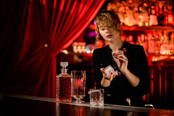 attractive female bartender breaks large piece of ice with ice pick to make cocktail
