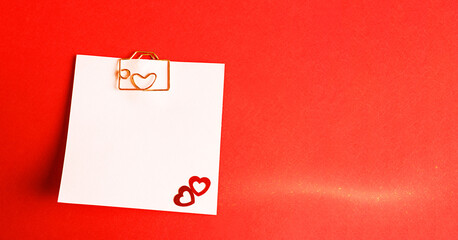 Square sheet for notes with a paper clip in shape of a letter and a heart. Decor of couples in love with hearts on a red background. Valentine's Day, message, greeting, declaration of love. Copy space