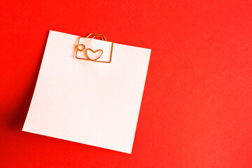Square sheet for notes with a paper clip in shape of a letter and a heart. Decor of couples in love with hearts on a red background. Valentine's Day, message, greeting, declaration of love. Copy space
