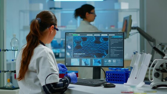 Laboratory doctor holding at blood sample and writing on computer while coworker opening door using digital computer with touch scan. Woman examining virus evolution using high tech and chemistry
