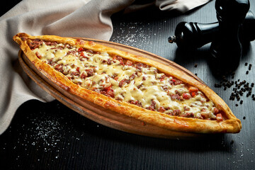 Turkish pide dish with slices of beef, tomatoes and cheddar cheese on black background