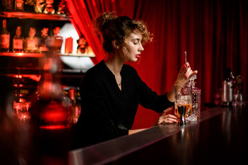 view of beautiful woman at the bar who is stirring cocktail in glass with spoon