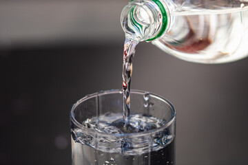Pouring water from plastic bottle into a glass on blurred background. Selective focus and copy space