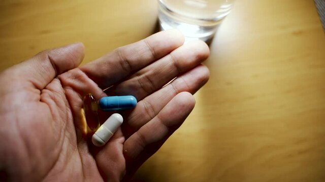 A hand with vitamins minerals and omega 3 supplement capsules next to a glass of water. A male person having health vitamin supplements displaying healthy lifestyle.