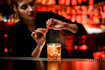woman bartender gently sprinkles on glass with cold alcoholic cocktail on the bar counter