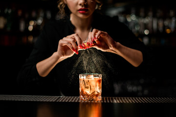 female bartender gently sprinkles on glass with cold alcoholic cocktail on the bar counter