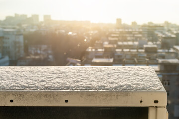 The snow on an outdoor air conditioning unit melting under the bright sunlight against blurred cityscape. Views from the 10th floor window. Early spring in the city.