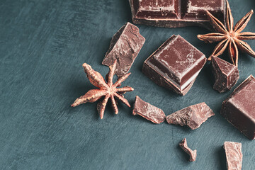 Chopped chocolate cubes and star anise on dark background with copy space, close-up view