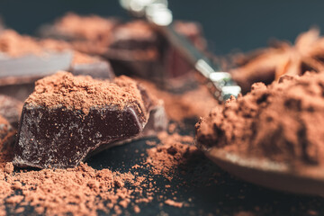 Chocolate chunk, chopped chocolate cubes with cocoa powder on dark background, close-up view