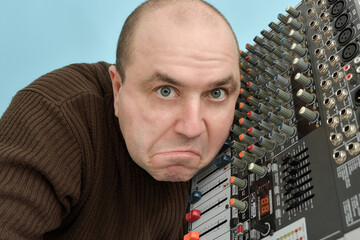 An inadequate man holds a music mixing console near his ear, thinking it is a tape recorder.