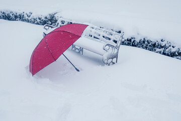Red umbrella on the snow, next to a bench.