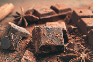 Chopped chocolate cubes with cocoa powder and star anise on dark background, close-up view